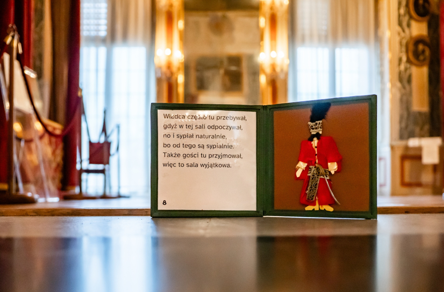Podłoga w Bibliotece Króla: trójkolorowa, iluzjonistyczna mozaika. Na niej otwarty przewodnik sensoryczny.
